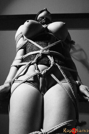 Hooded model Amely is trussed and draped by cords in an